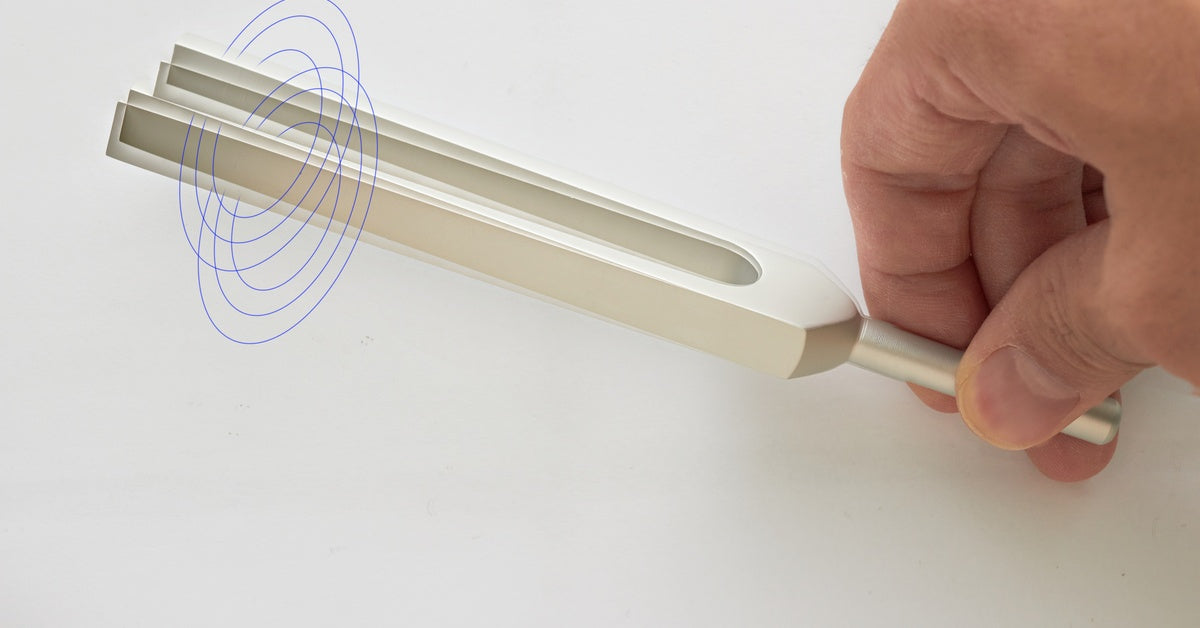 A close up of a person's hand holding up a tuning fork. Two blue swirl graphics encircle the top of the fork.