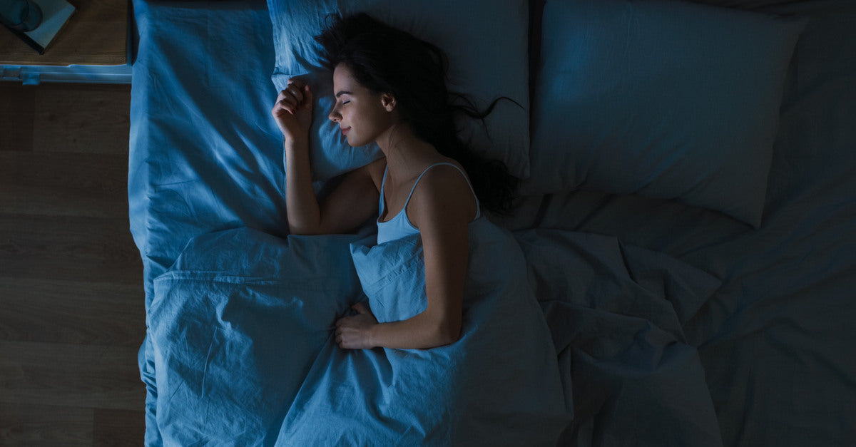 A woman lying on her side with her hand close to her face. She sleeps on her bed in her darkened bedroom.